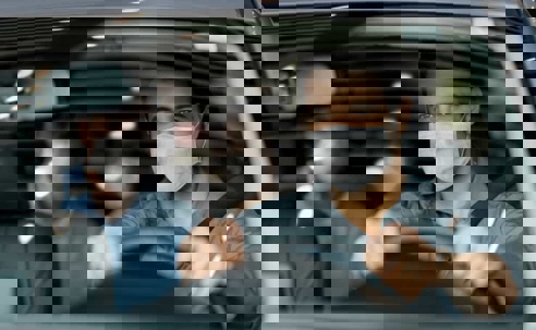 Rideshare driver wears disposable face mask while driving a masked couple sitting in the back seat