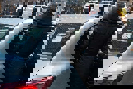 Woman in a long black coat and a gray beanie gets into the back seat of an Uber