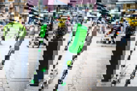 Close up of a Lime e-scooter that is stationary on a sidewalk in a metropolitan area