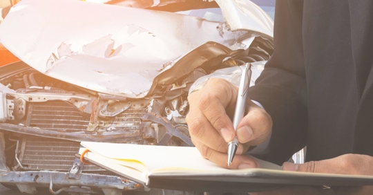 insurance adjuster writing on a pad in front of damaged car
